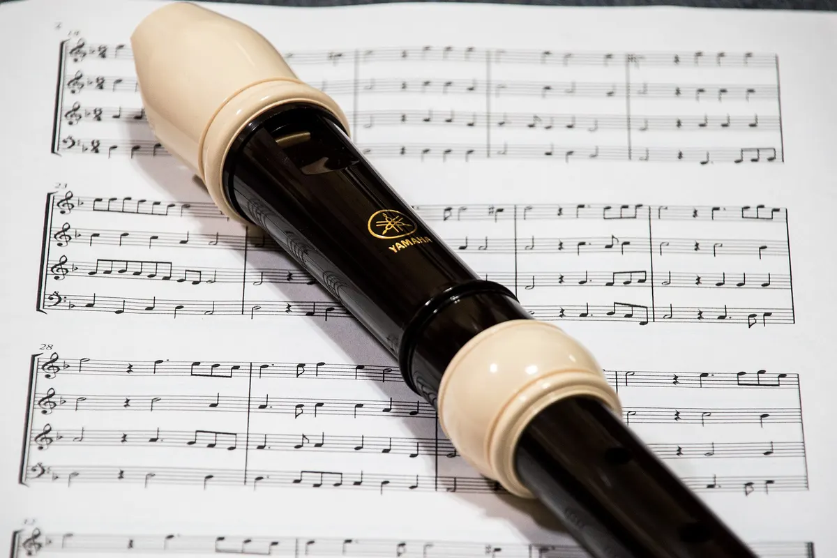 A black recorder lying across a page of sheet music