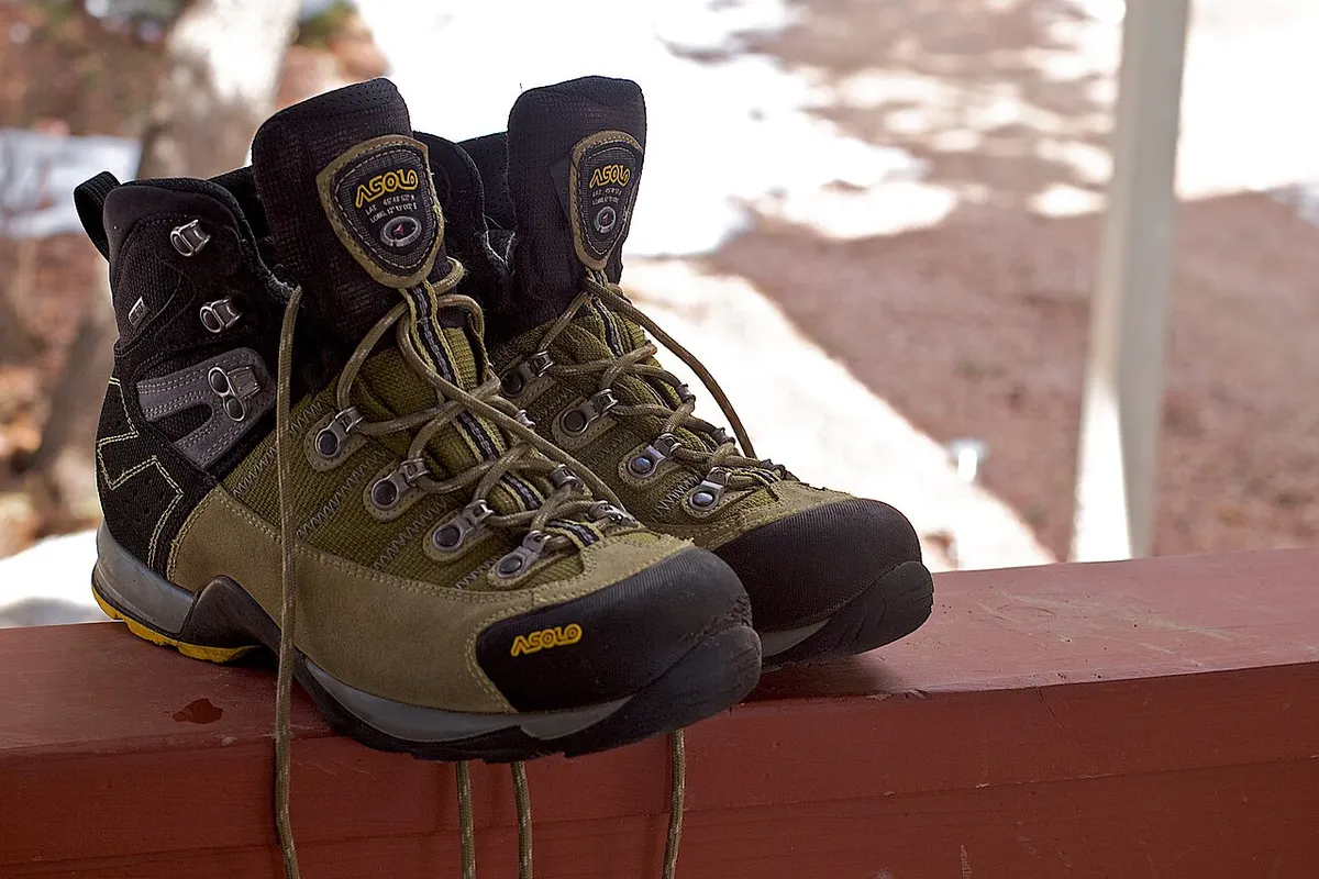 A pair of olive green hiking boots resting on a red wooden railing