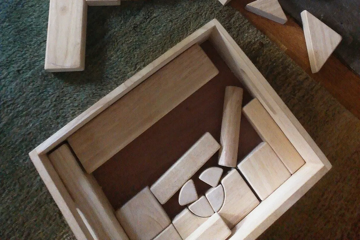 Two sets of wooden unit blocks scattered on a carpeted floor with their storage boxes